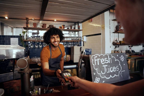 Retrato de garçom sorrindo segurando cartão de crédito furto máquina enquanto o cliente digitar código no café moderno — Fotografia de Stock