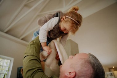 Genç baba evde oynarken çocuğu havaya kaldırıyor.