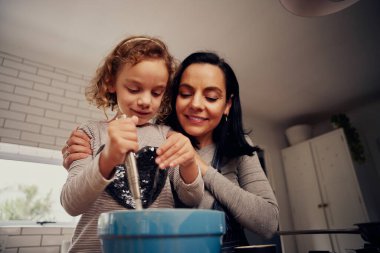 Anne ve kızın kâsede hamuru çırpışları ve mutfakta yemek pişirirken kâseye baharat katışları düşük açılı.