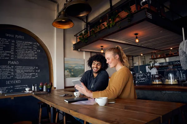 Joyeux jeune couple assis et relaxant dans un café en utilisant une tablette numérique pour regarder des vidéos — Photo