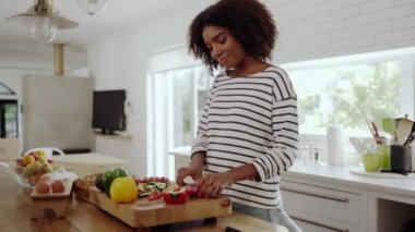 Genç bir kadın modern mutfakta tek başına kırmızı dolma biberi doğrama tahtasında bıçakla kesiyor.