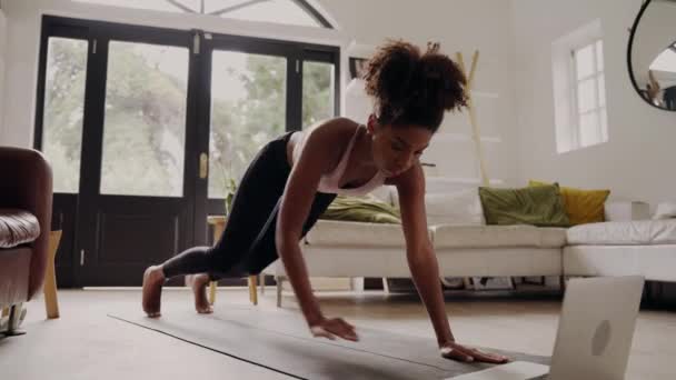 Sporty african woman working out on black mat while watching fitness video online on laptop at home — Stock Video