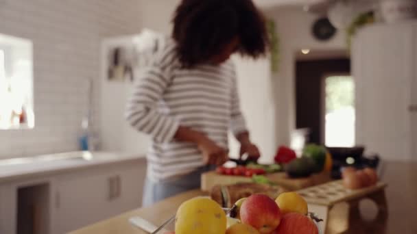 Молода жінка розрізає свіжі зелені кабачки на дерев'яній дошці на кухонній стійці — стокове відео