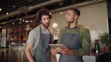 Modern kafede dijital tablet kullanarak yeni tariflere göz atan neşeli erkek garson.