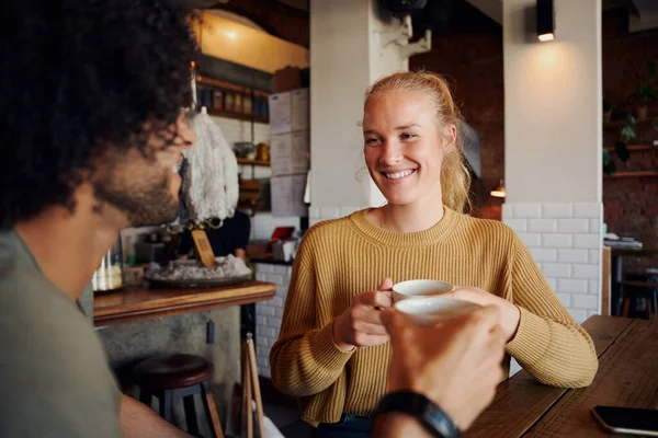 Retrato de una hermosa mujer joven sosteniendo taza de café y hablando con el hombre con el pelo rizado en la cafetería moderna —  Fotos de Stock