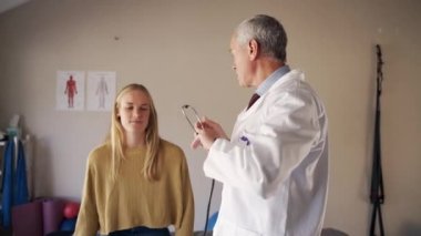 Üst düzey erkek doktor, kadın hastaların klinikte steteskop kullanarak nefes alışlarını dinliyor.