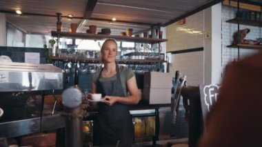 Gülümseyen sarışın kahve dükkanı sahibi bir müşteriye kahve fincanı veriyor.