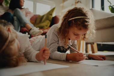 İki kızın portresi, evde kağıt üzerinde resim yaparken, ebeveynleri koltukta otururken.