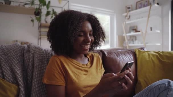 Uśmiechnięta afrykańska młoda kobieta dobrze się bawiąca rozmawiając w mediach społecznościowych odpoczywając na kanapie w domu — Wideo stockowe