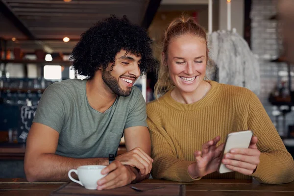 Joyeux jeune femme montrant drôle de vidéo dans le smartphone pour petit ami tout en se relaxant et assis dans un café moderne — Photo