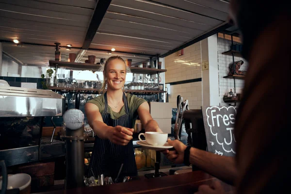 Beautiful young female waiter serving cup of coffee to customer in modern cafe — Stock Photo, Image