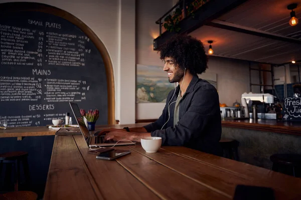 Gericht jonge mannelijke ondernemer typen op laptop met oortelefoon zitten in modern cafe — Stockfoto
