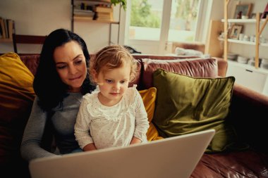 Genç anne ve kız kanepede oturup dizüstü bilgisayarla online alışveriş yaparak eğleniyorlar.