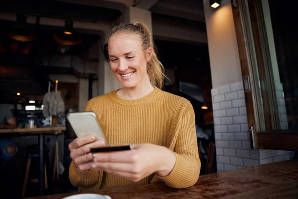 Donna felice in caffè effettuare il pagamento online con carta e smartphone in caffè — Foto Stock