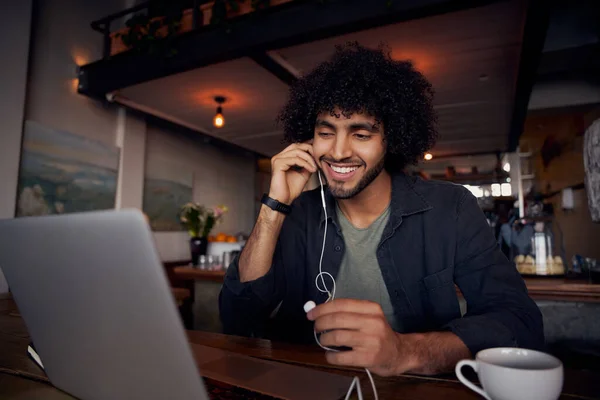 Knappe jongeman met krullend haar kijken video 's op laptop met oortjes in cafe — Stockfoto