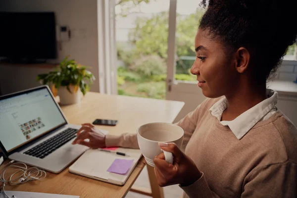 Portret van jonge vrouwelijke ondernemer die thuis op laptop werkt en koffie drinkt — Stockfoto
