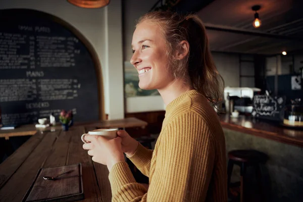 Sonriente joven hermosa mujer sosteniendo la taza de café en la cafetería mirando hacia otro lado — Foto de Stock