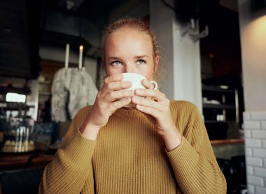Kafeteryada gözlerini kaçırıp kahve içen genç bir kadın.