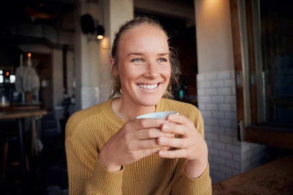 Retrato de una joven sonriente sosteniendo taza de café en la cafetería sentada y mirando hacia otro lado — Foto de Stock