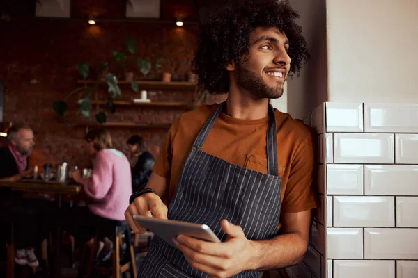 Porträtt av en glad servitör stående på restaurang lutande på väggen håller digital tablett — Stockfoto