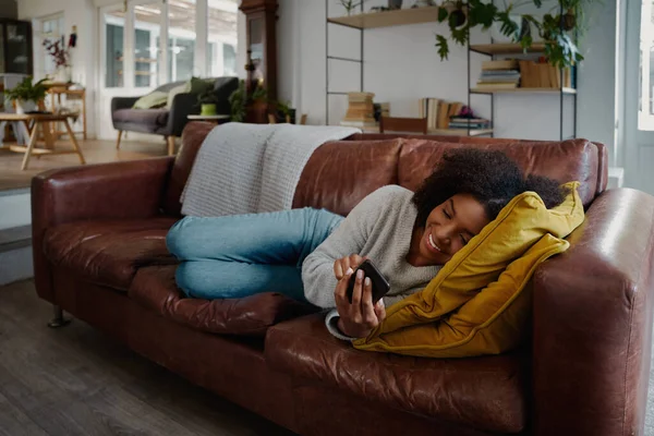 Африканська жінка лежить на дивані за допомогою смартфона під час смс - повідомлень. — стокове фото