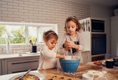 Küçük kız kardeşler modern mutfakta yumurta pişirmek için hamurdan zevk alıyorlar.