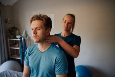 Genç bayan fizyoterapist klinikteki erkek hastaya boyun masajı yapıyor.