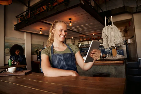 Garçom feminino sorridente em pé inclinado na mesa usando tablet digital no café moderno — Fotografia de Stock