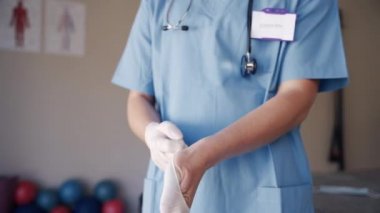 Rehabilitasyon merkezinde eline beyaz lastik eldiven takmış mavi üniformalı kadın bir fizyoterapist.