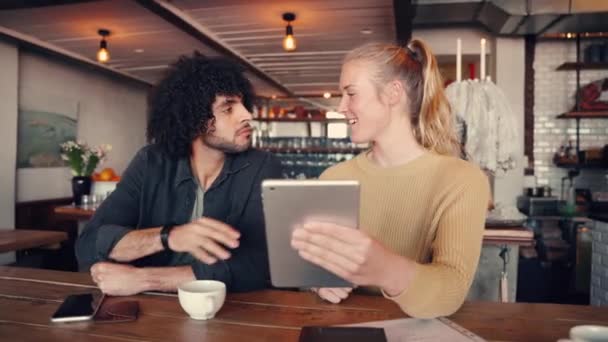Schöne blonde junge Frau zeigt ihrem Freund etwas auf digitalem Tablet im Café — Stockvideo