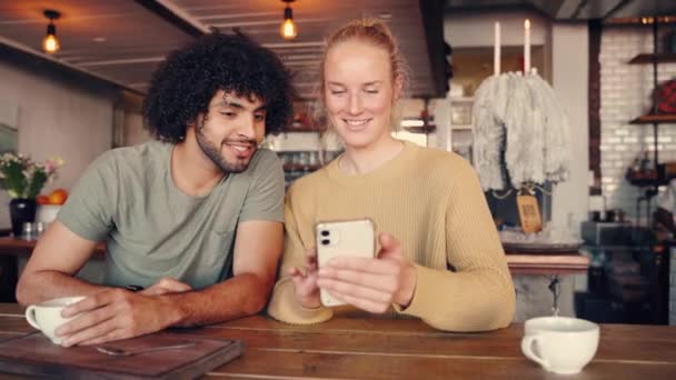 Giovane uomo ridere mentre seduto vicino fidanzata mostrando qualcosa di divertente sul suo smartphone — Video Stock