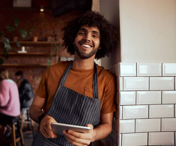 Duvara yaslanmış dijital tableti tutan mutlu bir erkek kafe sahibinin portresi.