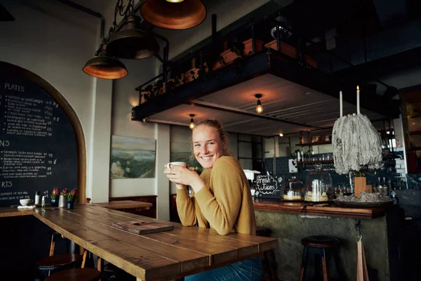 Porträt einer jungen schönen Frau, die im Café sitzt, sich entspannt auf einen Tisch lehnt und eine Kaffeetasse hält — Stockfoto