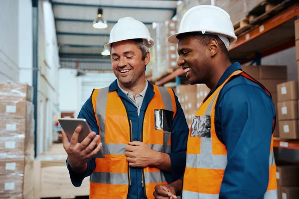 Engenheiros de fábrica multiétnicos sorrindo enquanto olham para a tela do tablet digital no armazém industrial — Fotografia de Stock
