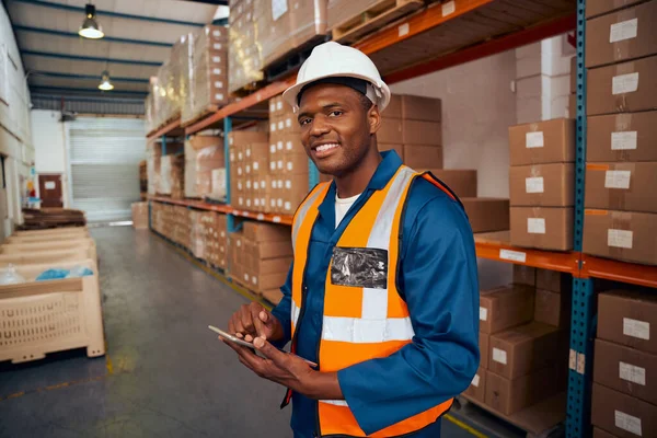 Glimlachend portret van een Afrikaanse magazijnmedewerker die een digitale tablet in de hand houdt en naar de camera kijkt — Stockfoto