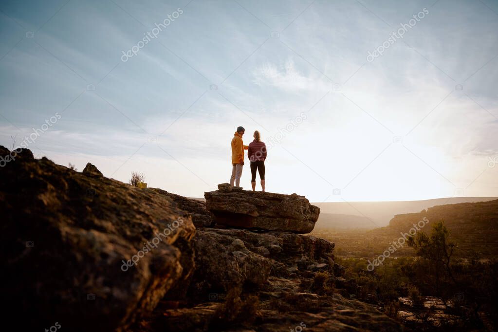 Rear low angle view of young couple friends standing on cliff edge looking at beautiful sunrise