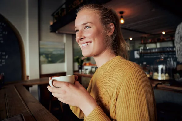 Mujer feliz sosteniendo la taza de café en un café moderno mirando hacia otro lado — Foto de Stock