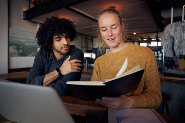 Jonge mannelijke en vrouwelijke zakenmensen op zoek naar notities in het dagboek tijdens het werken met behulp van laptop in moderne cafe — Stockfoto