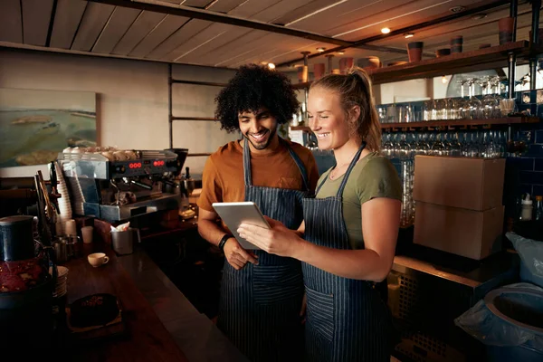 Leende servitör och servitris bär förkläde med digital surfplatta som står bakom disken på caféet — Stockfoto