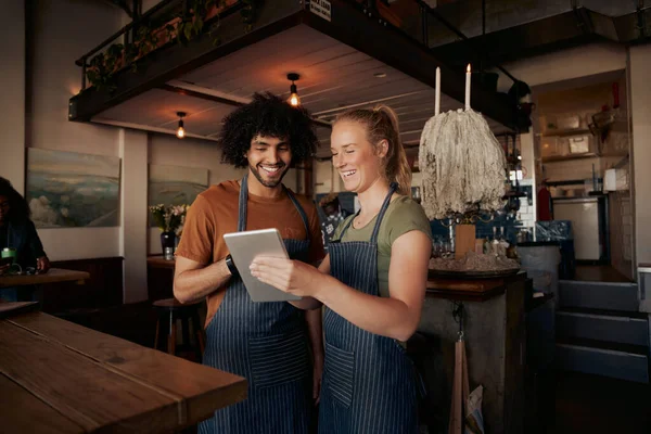Feliz colegas masculinos e femininos vestindo avental e rindo enquanto assiste vídeo em tablet digital no café — Fotografia de Stock