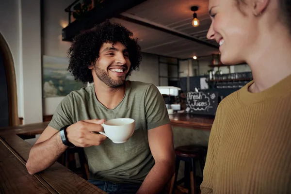 Przystojny młody mężczyzna z kręconymi włosami trzyma filiżankę kawy siedząc z piękną kobietą i rozmawiając w kawiarni — Zdjęcie stockowe