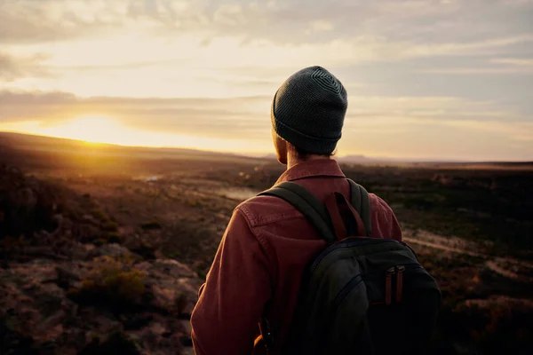 Achteraanzicht van de jongeman die op de klif staat en geniet van de zonsopgang kijkend naar de vallei en de bergen — Stockfoto