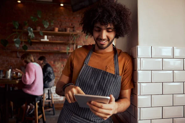 Jeune garçon serveur debout au restaurant appuyé sur le mur à l'aide d'une tablette numérique — Photo