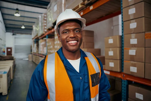 Glimlachend portret van een Afrikaanse jonge mannelijke arbeider in witte helm en uniform in magazijn — Stockfoto