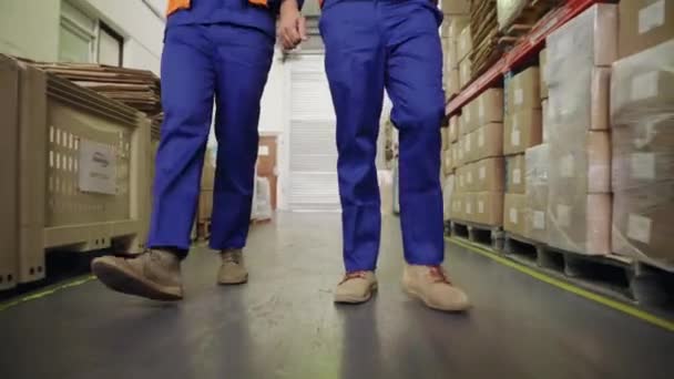 Gros plan des pieds de deux employés d'entrepôt marchant ensemble dans le passage entre les grands stocks de l'entrepôt — Video