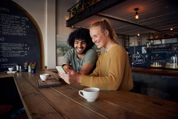 Couple souriant regardant smartphone assis dans un café moderne — Photo