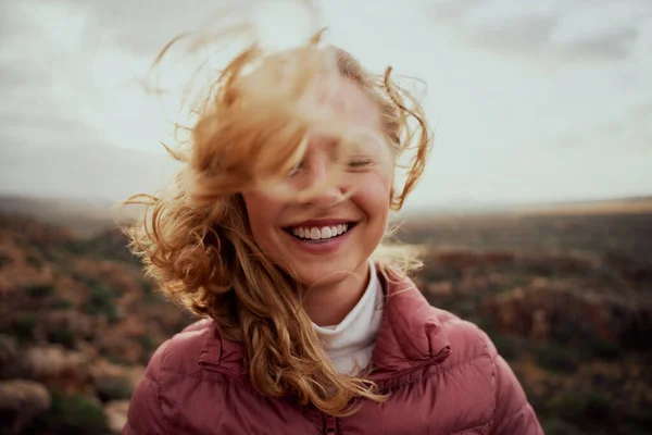 Genç gülümseyen kadının portresi kısmen rüzgarlı bir günde uçuşan saçlarla kaplı dağda dikilen kaygısız kadın.