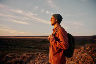 Sırt çantasıyla gezen mutlu yürüyüşçü başarılı bir şekilde dağın zirvesine ulaştıktan sonra güneşin doğuşunu seyrediyor.