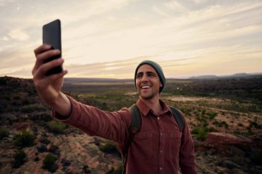 Portrait of happy young man taking selfie on smartphone against morning sunrise