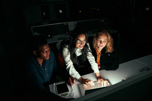 Equipe de negócios multiétnica bem sucedida trabalhando em laptop sobre mesa de escritório à noite — Fotografia de Stock